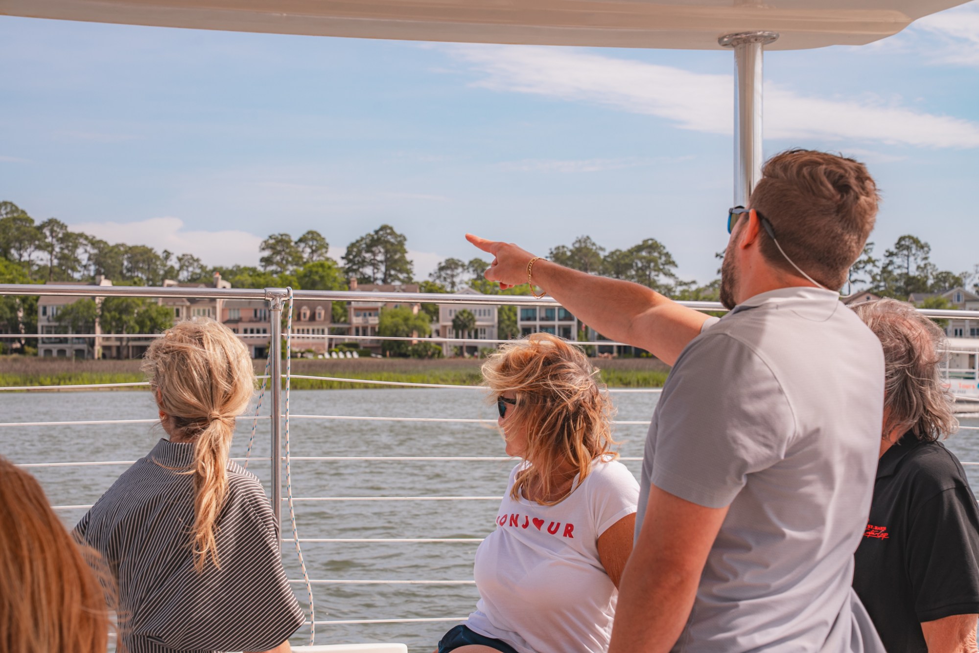 People on a boat looking at houses on the waterfront under a clear sky.