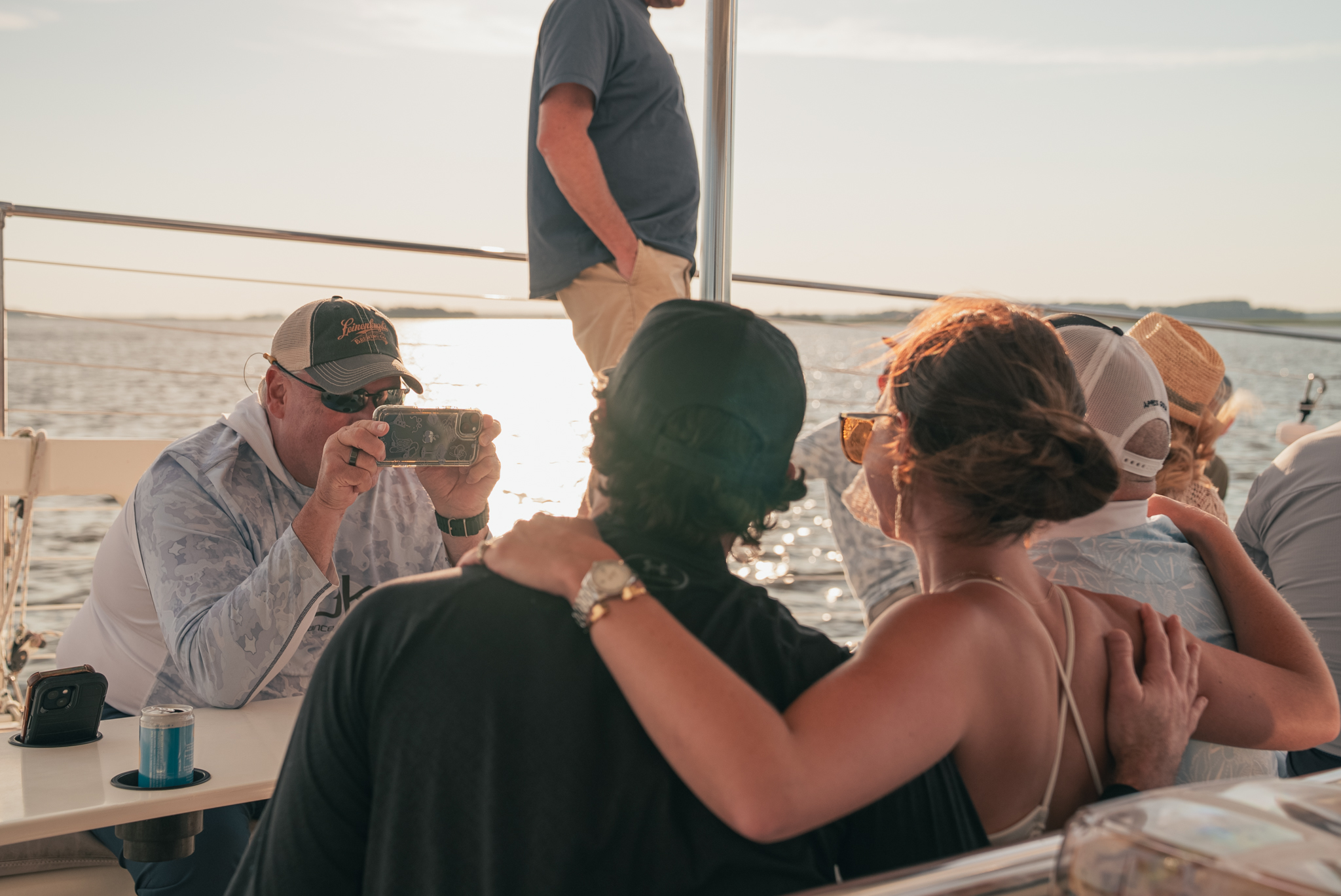 People sitting on a boat, with one person taking a photo, sunlight reflecting on the water.