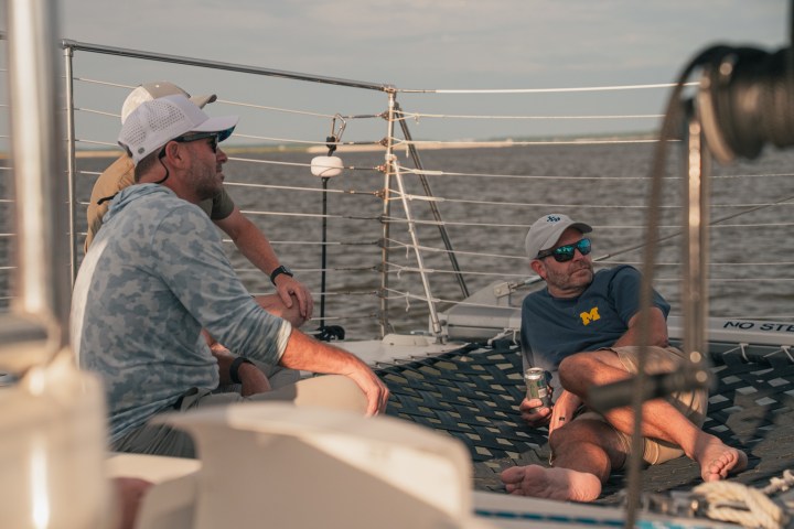Two men relaxing on a boat deck, wearing caps and sunglasses.