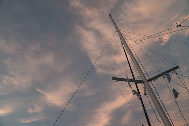 Sailboat mast with flags against a cloudy sunset sky.